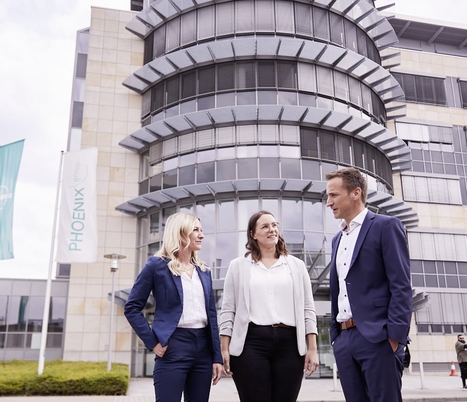 Ground-level view of the PHOENIX group headquarters in Mannheim: a modern office building with workers conversing in front, emphasizing the company's dynamic and collaborative environment.